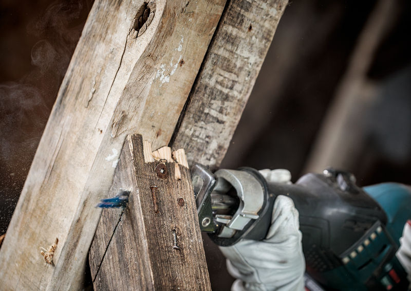 Eine Person mit Sicherheitsausrüstung verwendet eine Säbelsäge, um alte Holzbalken zu durchtrennen. Anwendungsbild