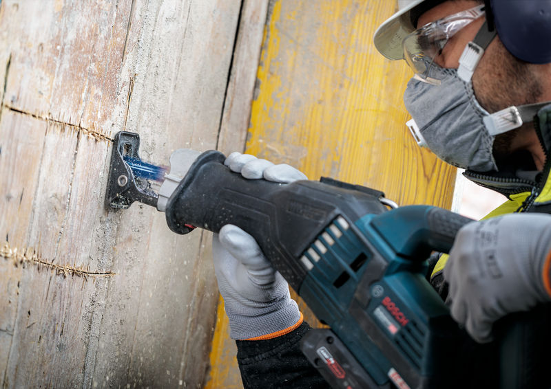 Eine Person mit Sicherheitsausrüstung sägt mit einer Säbelsäge einen Holzbalken durch. Anwendungsbild