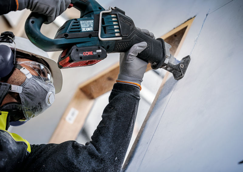Eine Person mit Sicherheitsausrüstung schneidet Trockenbauwände mit einer Säbelsäge. Anwendungsbild