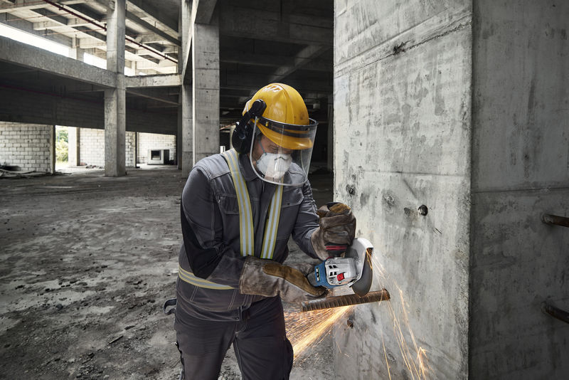 Eine Person mit Schutzausrüstung schneidet mit einem Akku-Winkelschleifer eine Metallstange. Anwendungsbild